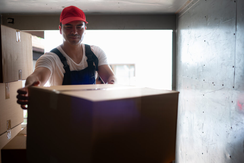 Handsome young delivery man in red cap and gloves holding a box